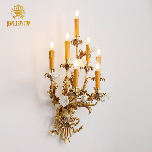 Close-up detail of the JEWELLERY TOP Versailles Septet brass wall sconce with seven candle bulbs and white ceramic flowers on a white wall.