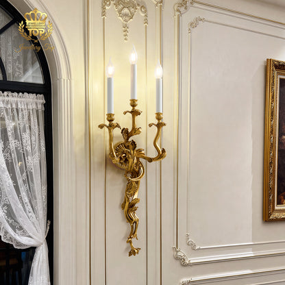 The Chloris Rococo brass wall sconce illuminated against a soft French cream wall by Jewellery Top.