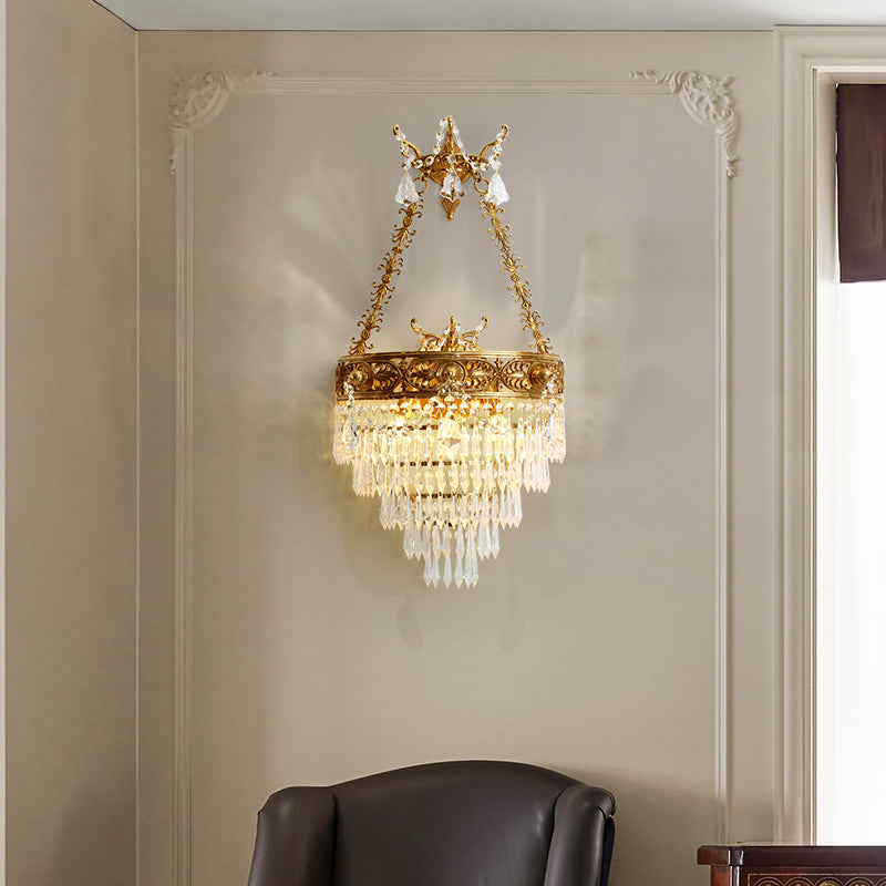Close-up front view of the ornate French brass wall lamp with intricate scrollwork and a waterfall of crystal beads.