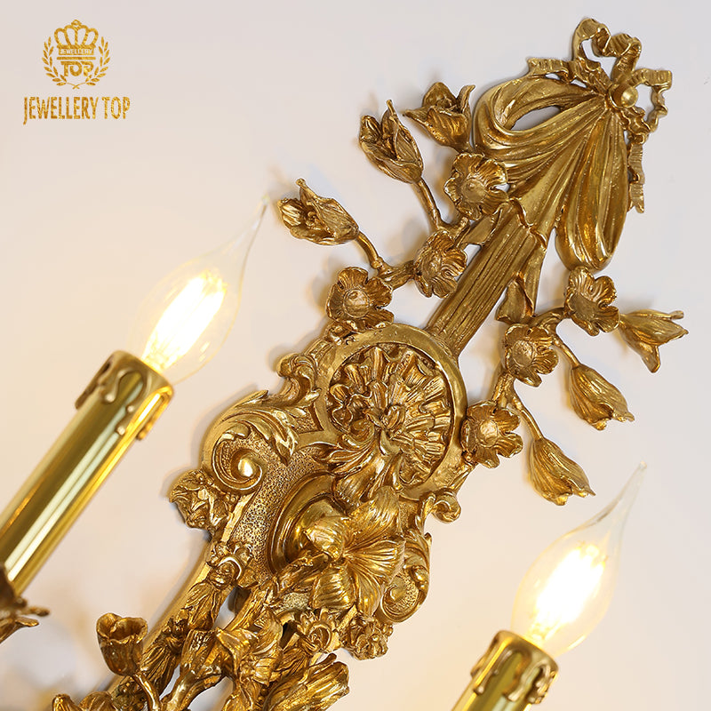 Extreme close-up macro detail of the sconce’s central brass bow decoration and surrounding leaf motifs.