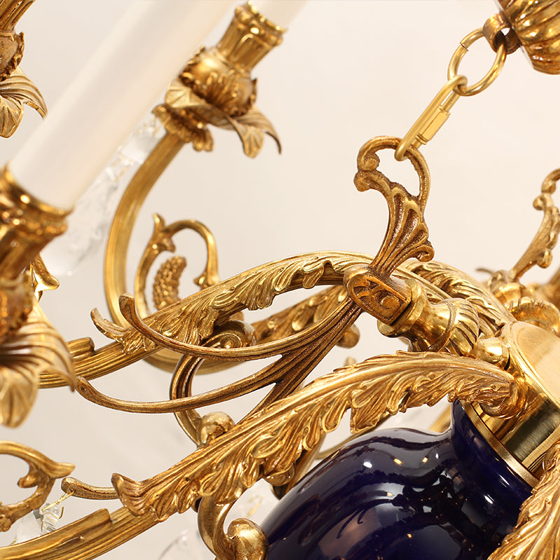 Detailed shot of intricate brass scrollwork, a candle bulb, and blue ceramic on a chandelier arm.