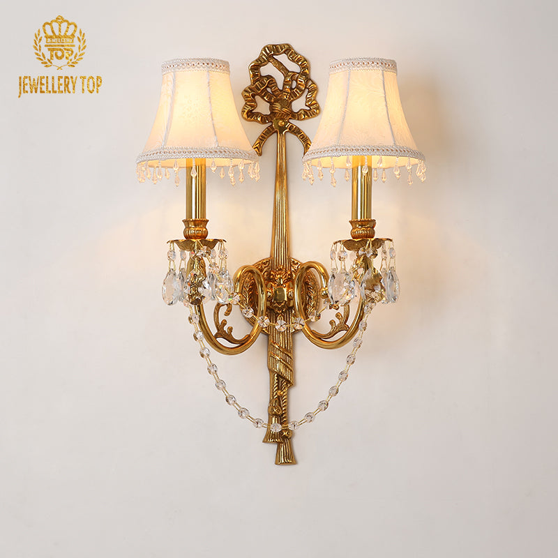 Detailed product shot of the JEWELLERY TOP branded brass sconce with white shades, central knot, and crystal fringe.