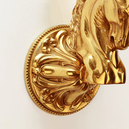 Detailed shot of the ornate, leaf-engraved circular wall mount and the connection point of the brass column on the wall lamp.