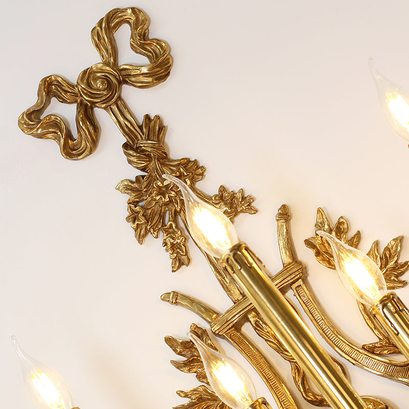 Close-up macro detail of the ornate brass bow, vine, and leaf decorations on the wall light.