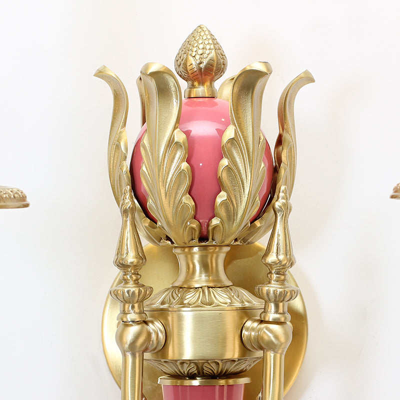 Close-up macro detail of the pink ceramic blossom and teal leaf decorations on the brass sconce.