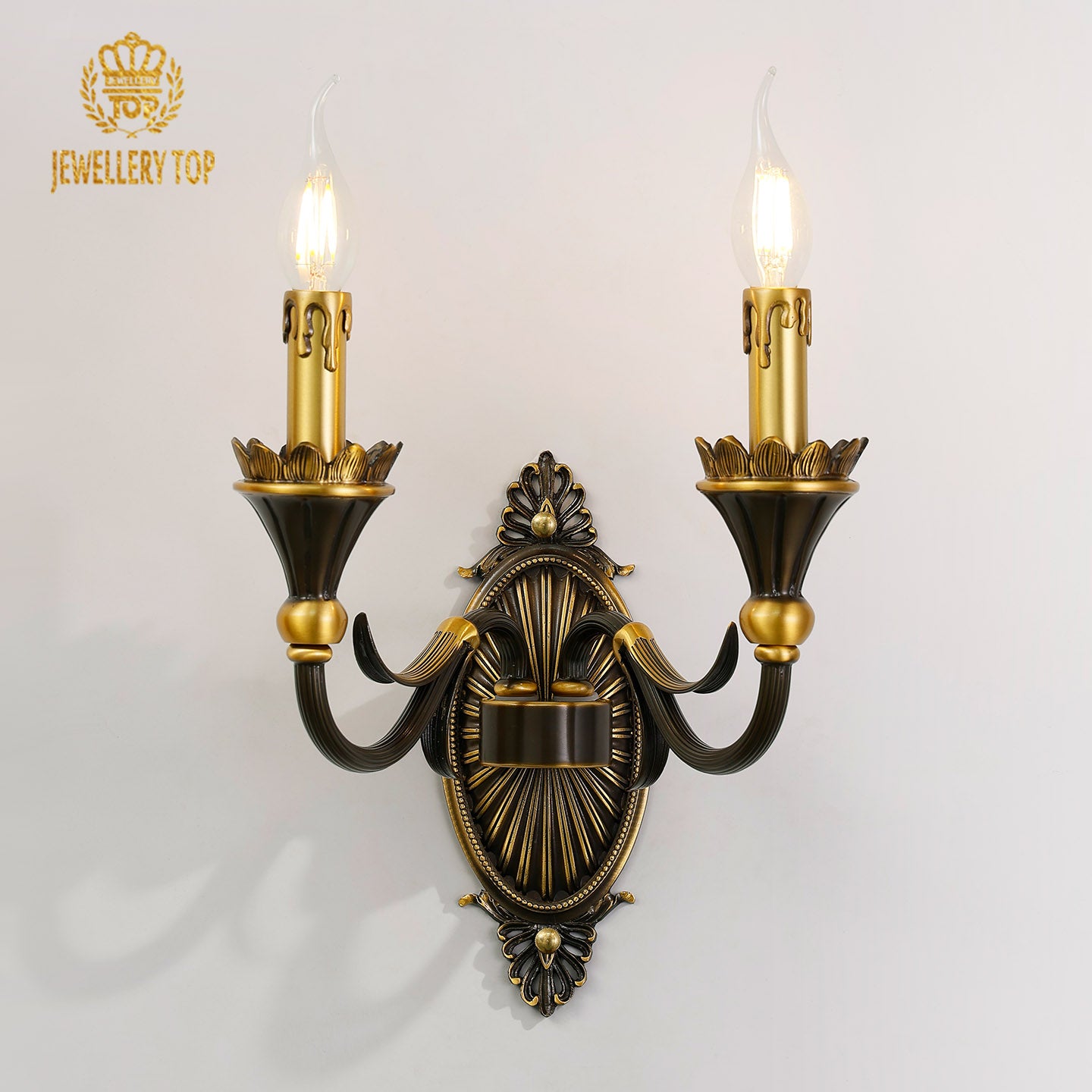 Front view of the JEWELLERY TOP Radiant Fleur-de-Lys brass wall sconce with two candle arms on a white wall.
