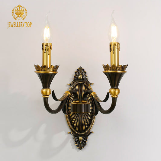 Front view of the JEWELLERY TOP Radiant Fleur-de-Lys brass wall sconce with two candle arms on a white wall.