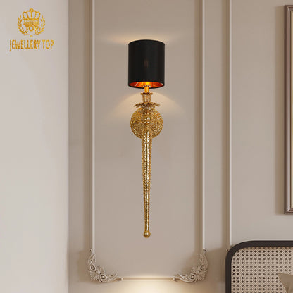 Classical brass sconce with black lampshade installed on a beige wall with white molding, emitting warm downlight.