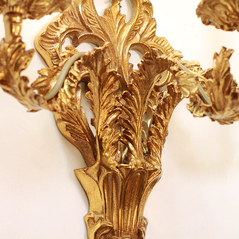 Macro detail of the central brass sunburst medallion and Baroque leaf carvings on the wall light.