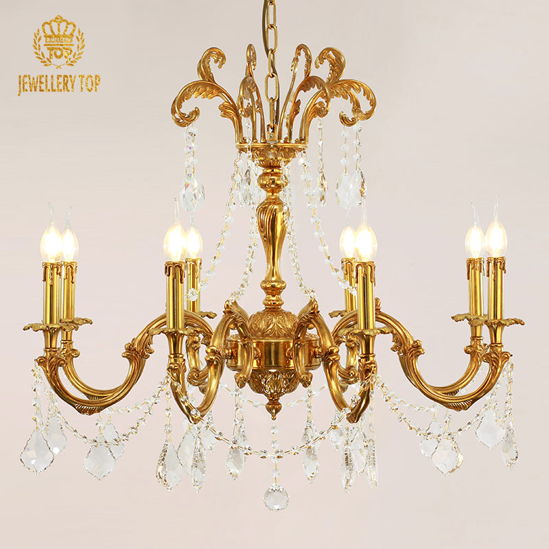 Front view of a JEWELLERY TOP branded brass crystal chandelier against a light wall.