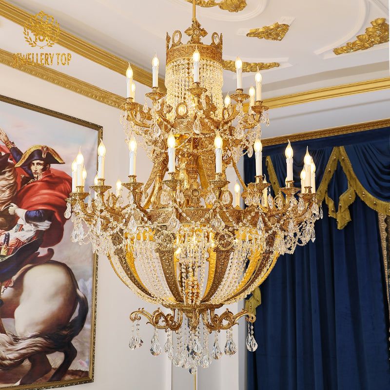 Large brass chandelier installed in a hotel lobby with blue curtains and classical painting.