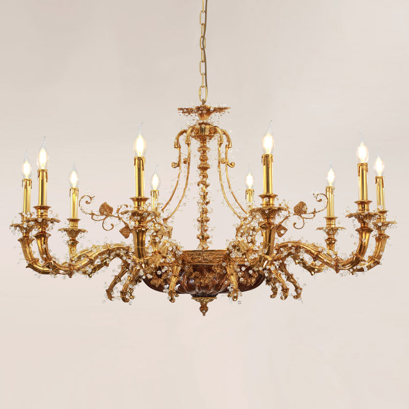 A lit European classical brass chandelier with golden finish and crystal accents against a light wall.
