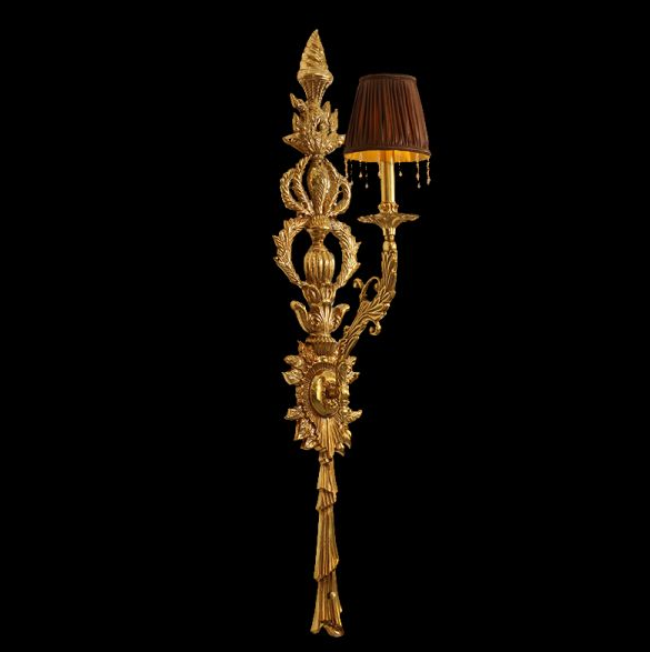 Close-up detail of the shield-shaped brass medallion with classical figure and scrollwork on the wall light.