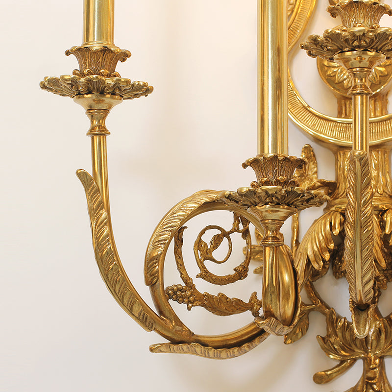 Extreme close-up of a curved brass arm with textured leaf veins and a classic candle-style bulb holder.