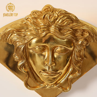 Close-up macro detail of the Medusa head on a golden brass wall light, with brand logo JEWELLERY TOP.