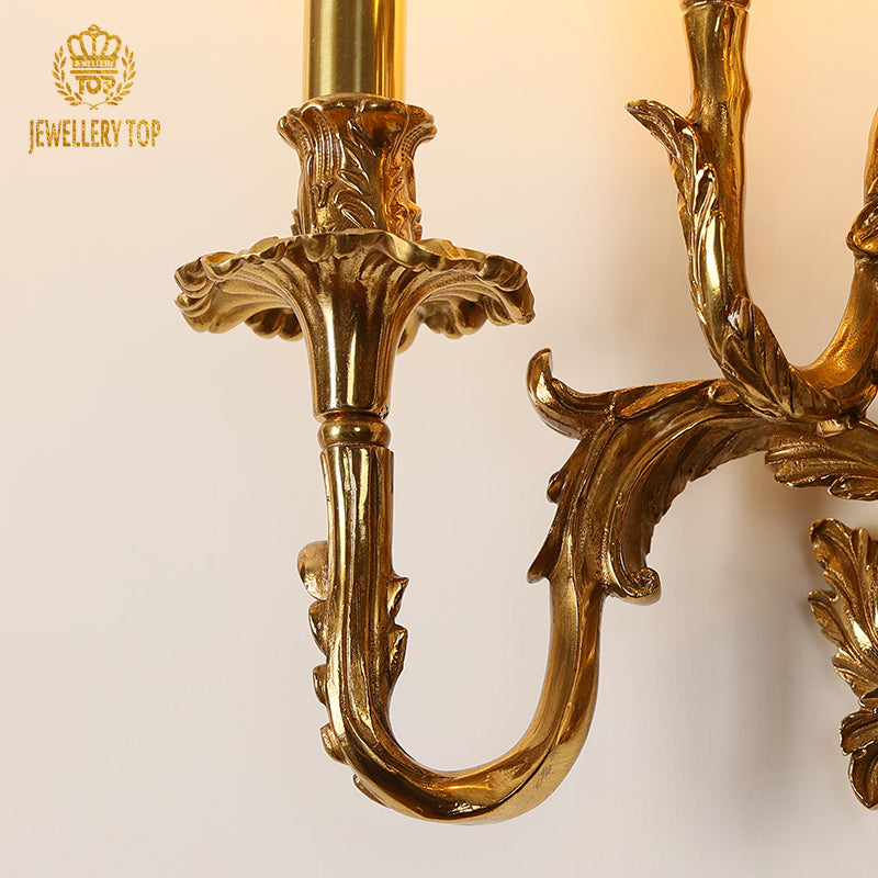 Extreme close-up of a single curved brass arm, featuring deep-relief floral engraving and polished surface.