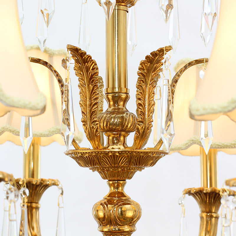 Macro close-up of a brass arm with leaf engraving, a pleated fabric shade, and hanging crystal prisms.