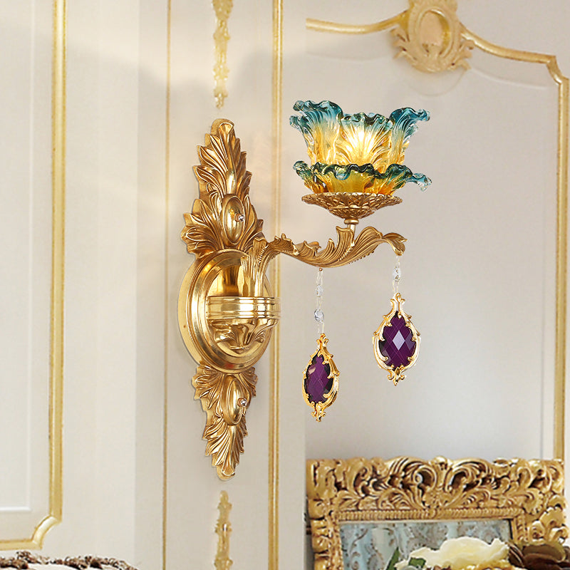The retro brass wall lamp installed on a white and gold-accented wall, emitting a warm, colorful glow.