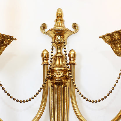 Macro close-up of the sconce’s detailed urn finial, bead chains, and floral engraving on the brass.