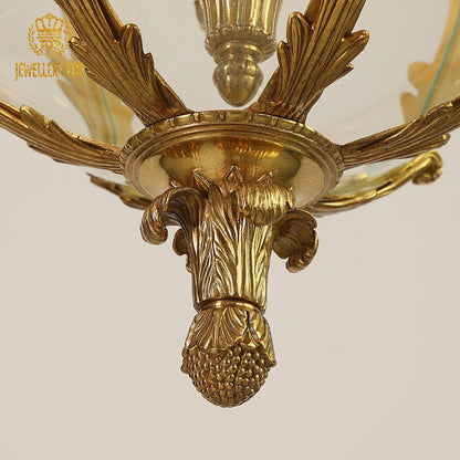 Macro detail of fruit cluster carvings and flared glass shades on a classical brass pendant light.