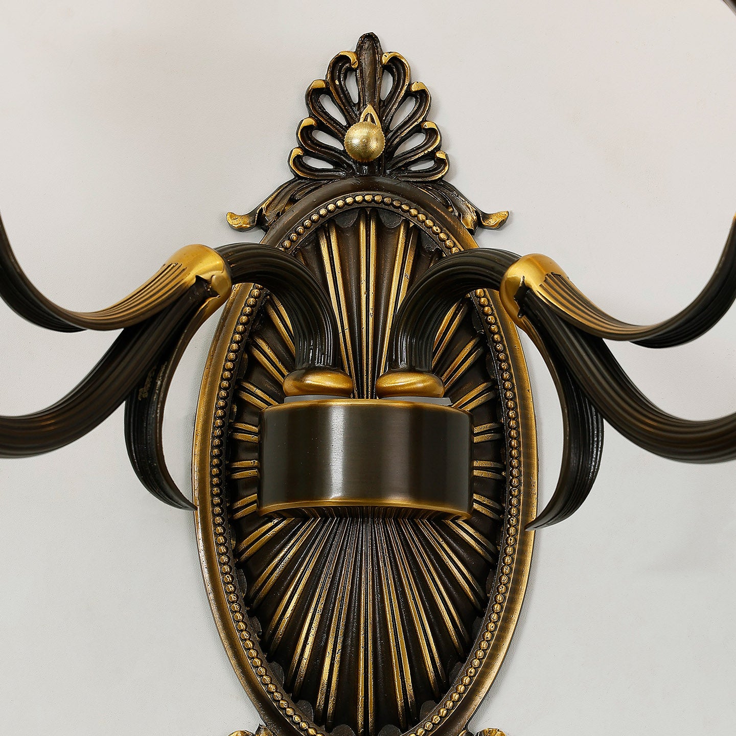 Extreme close-up macro detail of the sconce's central oval medallion with sunburst pattern and intricate scrollwork.