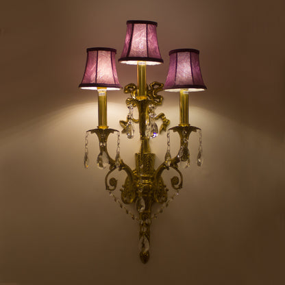 The Victorian-style brass wall lamp installed on an elegant dark blue wallpapered wall.