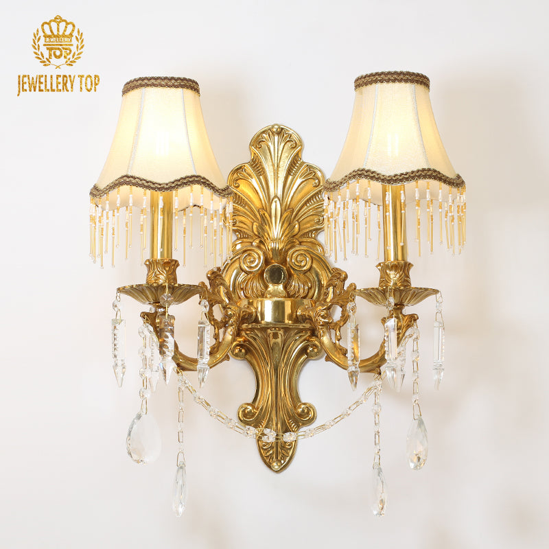 Front view of the ornate golden wall sconce with lit fabric lampshades, isolated on a dark background.