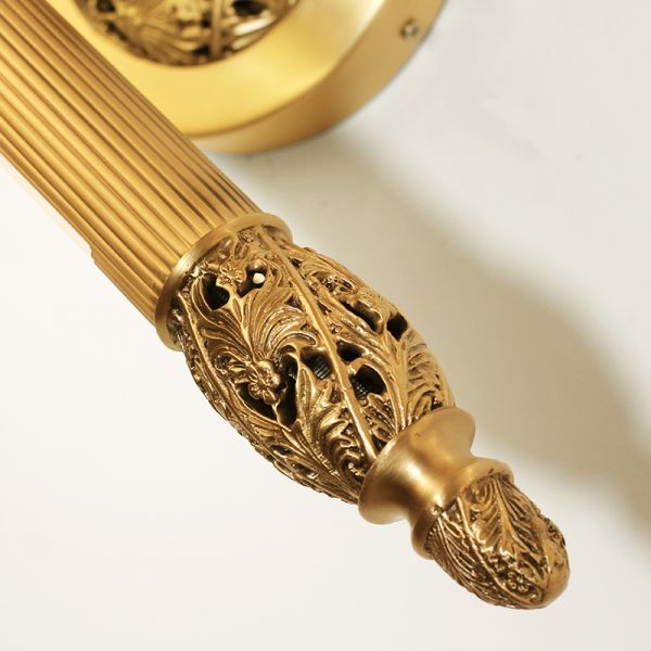 The linear brass wall sconce in a classic interior, mounted beside an ornate gold-framed mirror reflecting flowers.