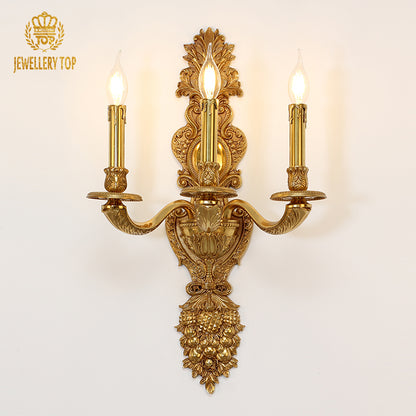 JEWELLERY TOP branded antique bronze wall light, showcasing three illuminated bulbs and intricate metalwork on white.