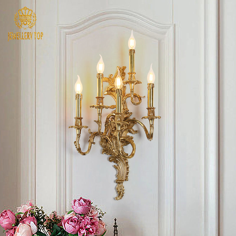 The luxury brass villa wall light installed on a light wall, emitting a warm glow beside pink peonies and decor.
