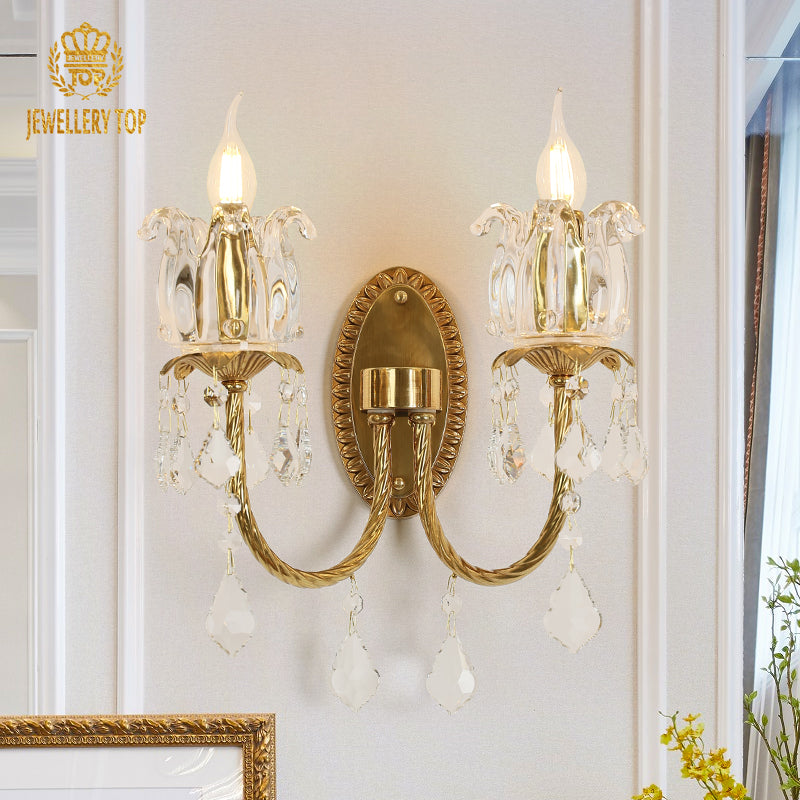 The classical brass wall lamp with JEWELLERY TOP branding, showcasing lit candle bulbs and crystal details on a white background.