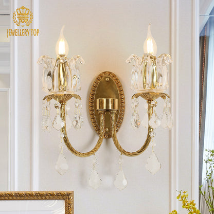 The classical brass wall lamp with JEWELLERY TOP branding, showcasing lit candle bulbs and crystal details on a white background.