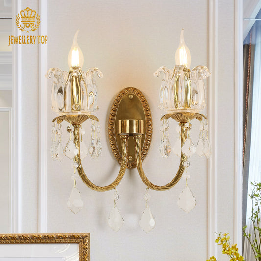 The classical brass wall lamp with JEWELLERY TOP branding, showcasing lit candle bulbs and crystal details on a white background.
