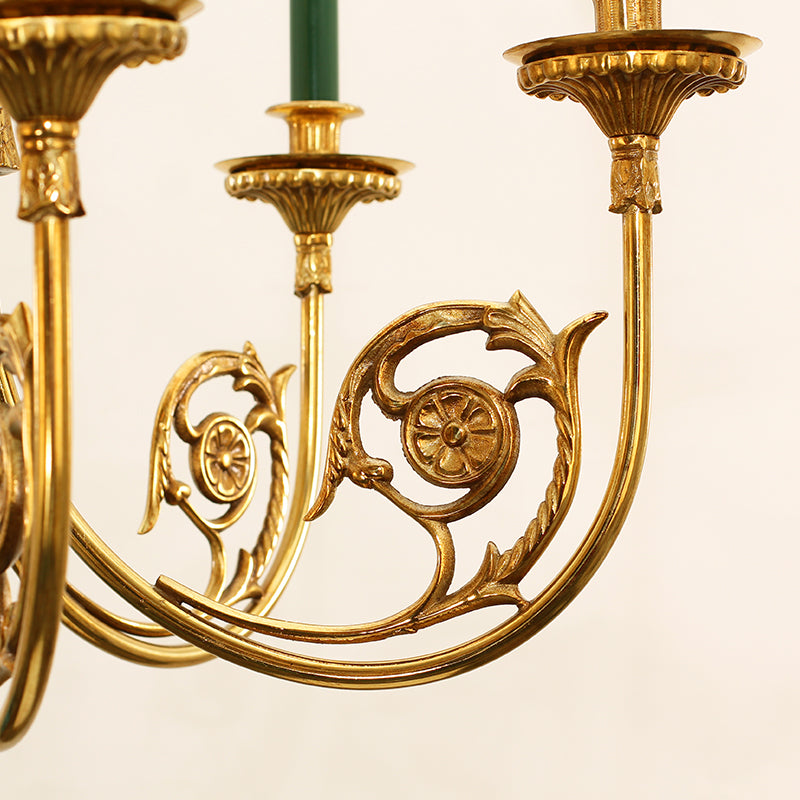 Close-up detail of a brass chandelier arm showing green bulb and ornate scrollwork.