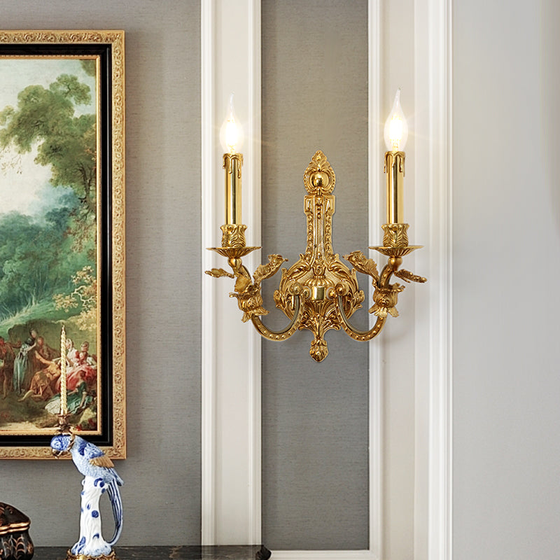 The installed French brass wall lamp on a light wall, beside a gold-framed painting and blue-white ceramic vase.