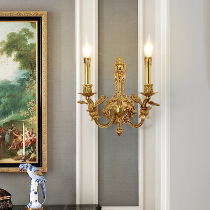 The installed French brass wall lamp on a light wall, beside a gold-framed painting and blue-white ceramic vase.