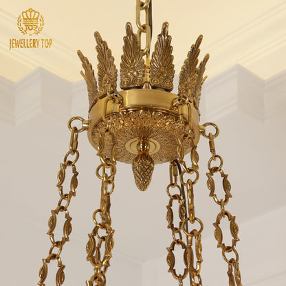 Detail of the chandelier's ornate brass base with wing-like scrolls and pinecone finial.