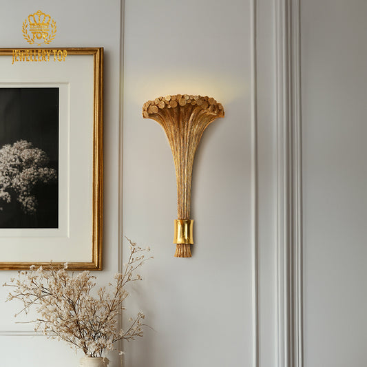 The antique bronze French wall sconce installed on a white wall next to framed art and a dried floral arrangement.