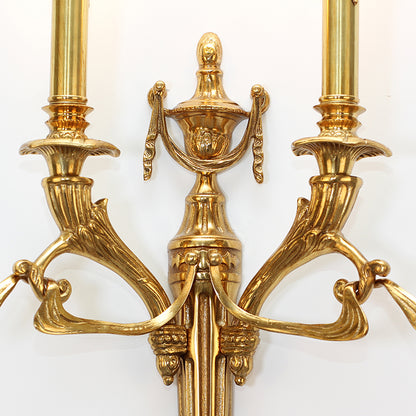 Macro shot of the wall lamp’s central urn decoration and finely engraved floral patterns on the brass surface.