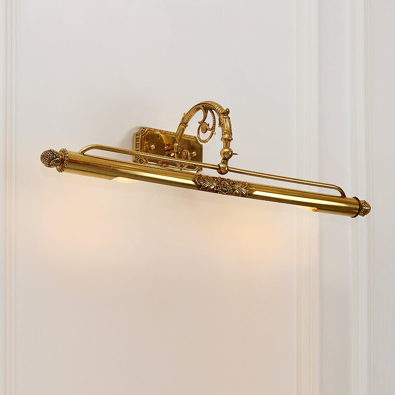 The brass mirror sconce light mounted on a white wall, emitting a soft downward glow onto a decorative gold-framed picture.