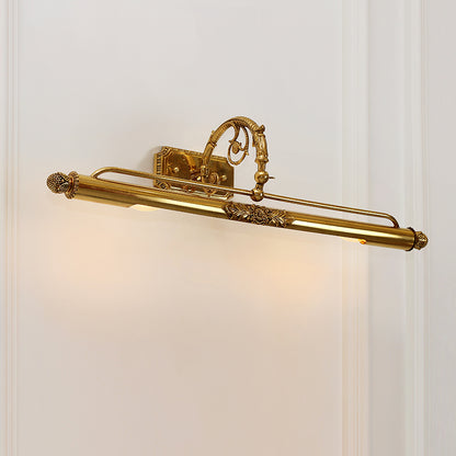 The brass mirror sconce light mounted on a white wall, emitting a soft downward glow onto a decorative gold-framed picture.