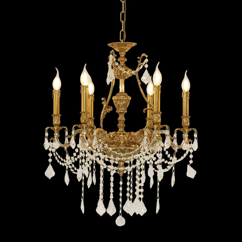 A golden brass chandelier with crystal strands, suspended by chains against a plain wall.