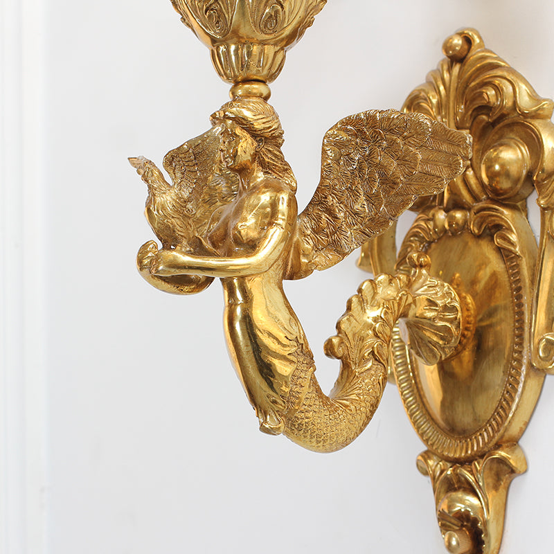 Extreme close-up of the guardian angel figure with wings, holding a small bird, on the luxury brass wall lamp.