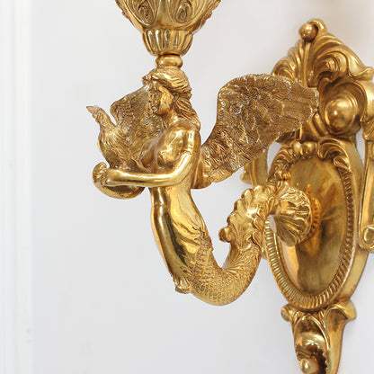 Extreme close-up of the guardian angel figure with wings, holding a small bird, on the luxury brass wall lamp.
