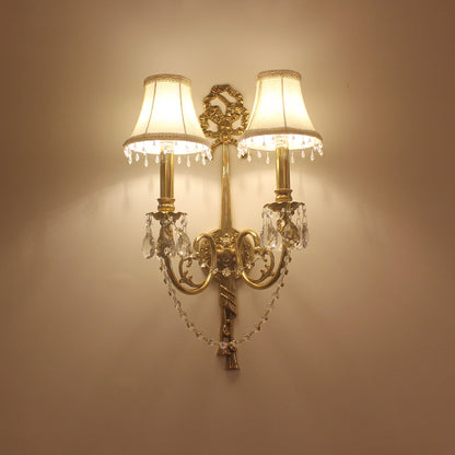 The installed Victorian wall light on a beige wall, emitting a warm glow with crystal tassels and ornate arms.