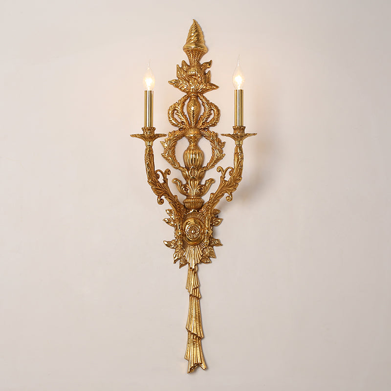 The French bronze wall light mounted on a clean white wall, highlighting its symmetrical candle-style arms and central spire.