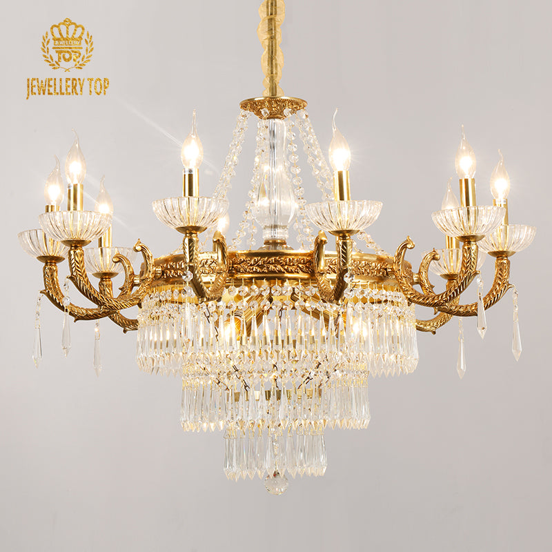 JEWELLERY TOP branded golden brass and crystal chandelier against a light grey wall.