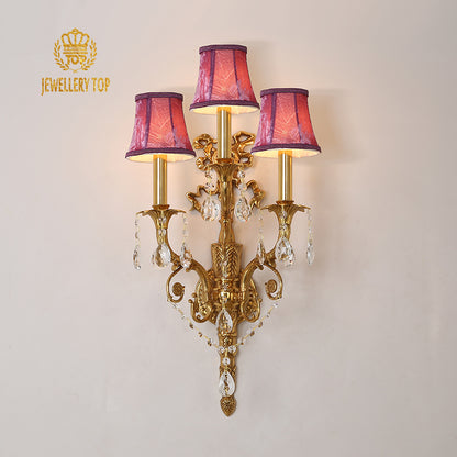 JEWELLERY TOP branded decorative wall lamp with intricate golden scrollwork and lit bulbs.