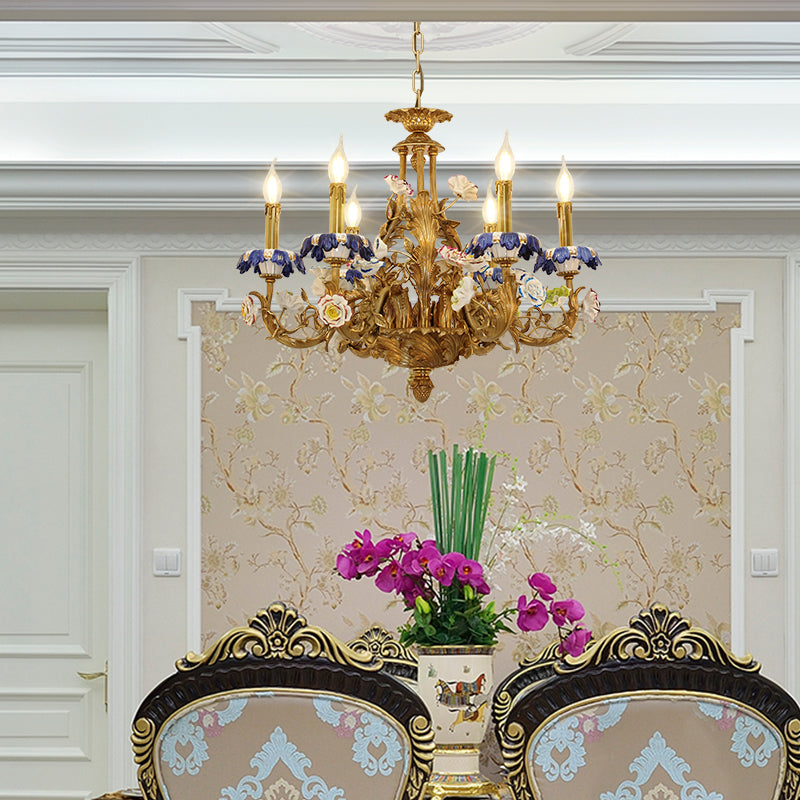 The brass and porcelain chandelier installed above dining chairs in an elegant floral-wallpapered room.