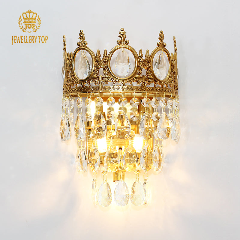 Extreme detail shot of the sconce’s ornate brass crown structure and the suspended teardrop crystal centerpieces.